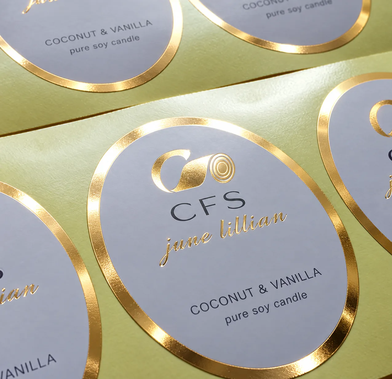 Gold cold-foil candle labels with metallic foil rims and script lettering on a sage green printed label sheet