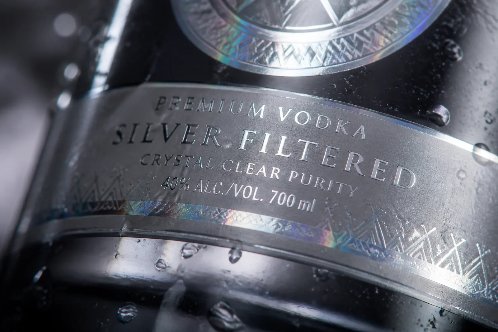 Macro close-up of a cold foil printed silver label on a premium vodka bottle, showing crisp metallic ink and fine micro-typography under studio lighting